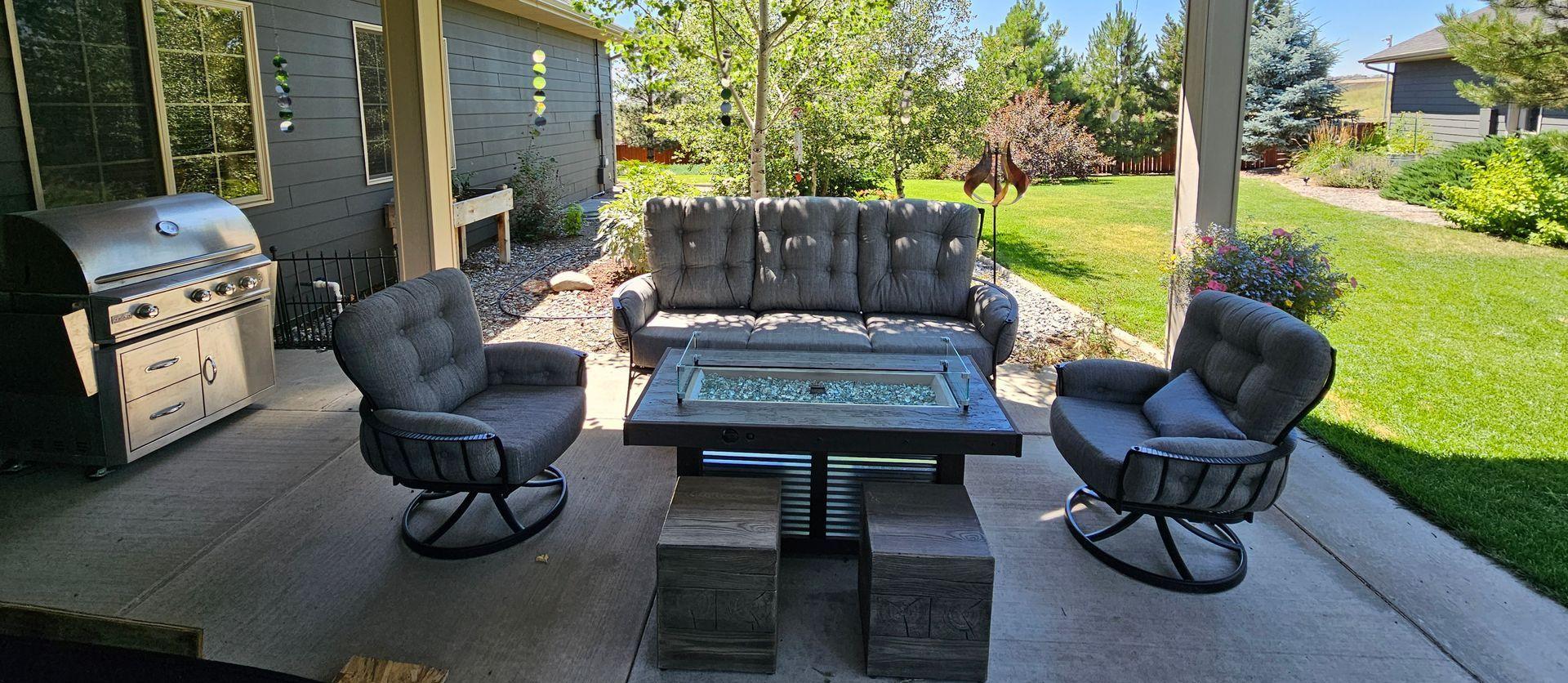 Backyard patio with a stainless grill, swivel chairs and a fire table beside the lawn